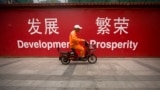 FILE - A maintenance worker rides a scooter past banners reading "Development" and "Prosperity" in English and Chinese on a street in central Beijing, July 15, 2015.