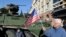 Чоловік тримає прапорець США біля американської броньованої машини Stryker з конвою військ НАТО під час зупинки для зустрічі з місцевими жителями в Білостоку, Польща. 24 березня 2015 р.