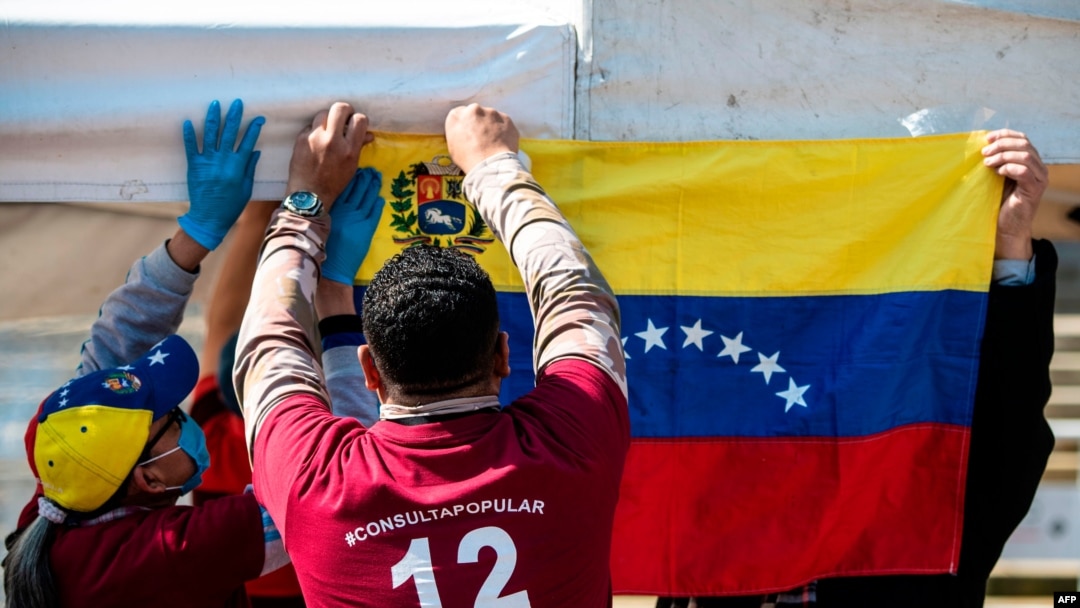 Migrantes venezolanos cuelgan una bandera nacional venezolana durante una "consulta popular" convocada por el líder de la oposición venezolana Juan Guaidó en Bogotá, el 12 de diciembre de 2021.
