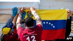 Migrantes venezolanos cuelgan una bandera nacional venezolana durante una "consulta popular" convocada por el líder de la oposición venezolana Juan Guaidó en Bogotá, el 12 de diciembre de 2021.