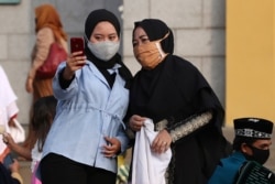 Muslim women wearing face masks as precaution against the new coronavirus outbreak, take a selfie after an Eid al-Adha prayer at a mosque in Jakarta, Indonesia, July 31, 2020.