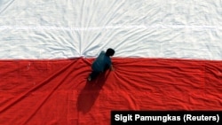 Seorang pria mempersiapkan bendera raksasa sebelum mengibarkannya pada perayaan hari kemerdekaan di Universitas Kristen Petra di Surabaya, Jawa Timur. (Foto: REUTERS/Sigit Pamungkas)