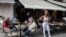 A cafe-restaurant employee stands outside as people drink coffee in Monastiraki district of Athens, May 25, 2020, as Greece restarted regular ferry services to its islands, and cafes and restaurants were also back open for business. 