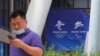 资料照：2021年7月30日，在北京奥组委总部，一名男子在走过北京2022年冬奥会和冬残奥会的标志时使用手机。