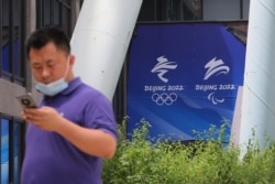 FILE - A man uses his phone as he walks past signs of the Beijing 2022 Olympic and Paralympic Winter Games at the headquarters of Beijing Organizing Committee, in Beijing, China, July 30, 2021.