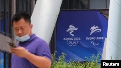 FILE - A man uses his phone as he walks past signs of the Beijing 2022 Olympic and Paralympic Winter Games at the headquarters of Beijing Organizing Committee, in Beijing, China, July 30, 2021. 