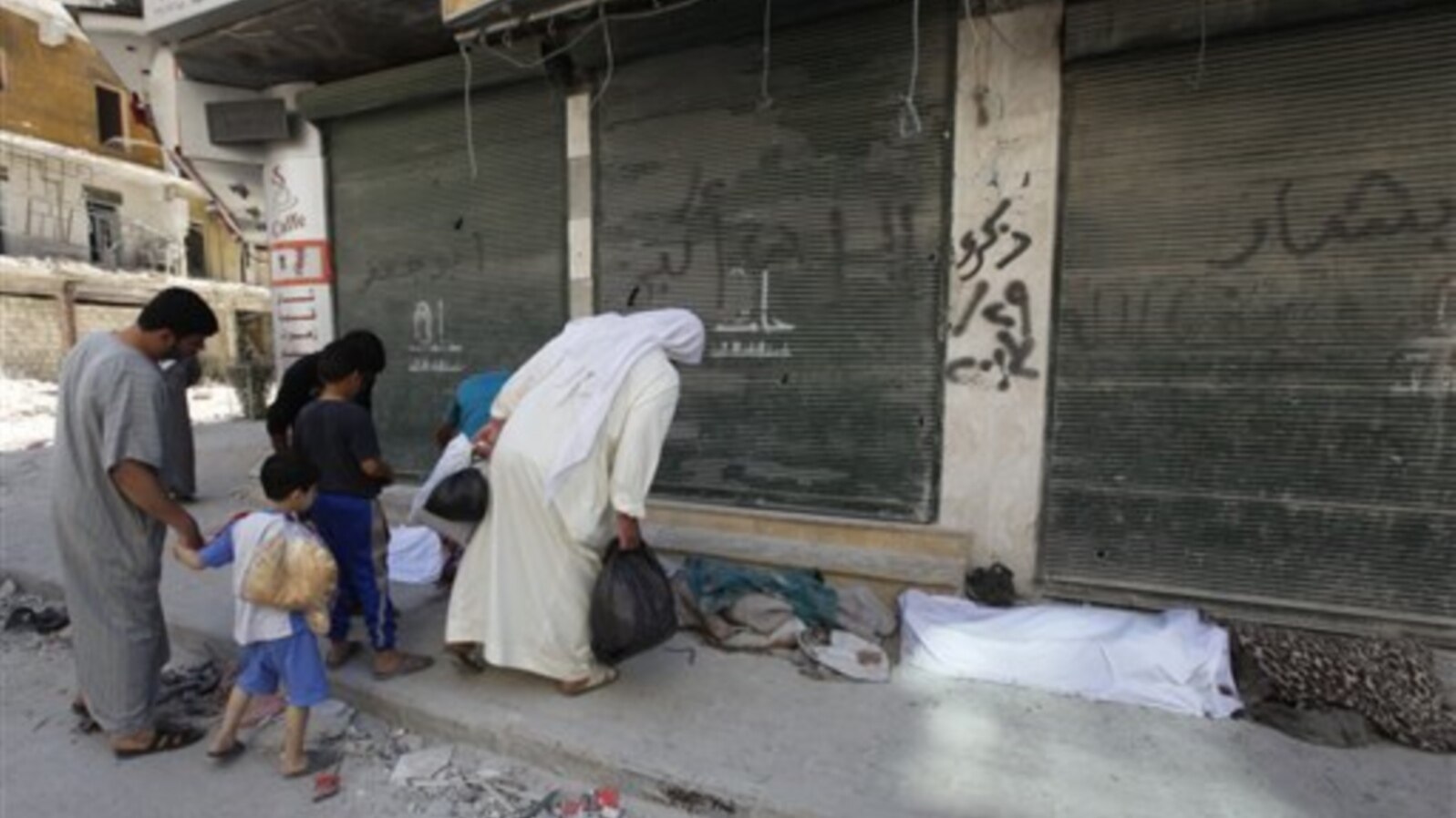 Syrian citizens look at dead bodies on a roadside in front of al-Shifa hospital, al-Shaar neighborhood, Aleppo city, Sept. 24, 2012.