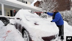 A woman shovels snow off her car in a driveway in Port Washington, New York, Jan 27 2011
