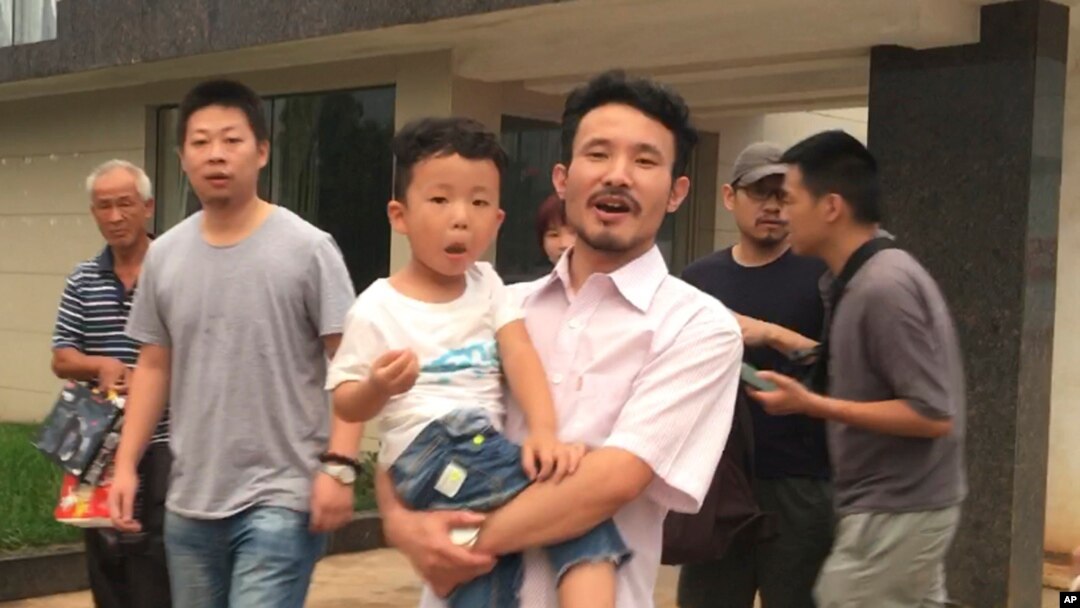 This image taken from video shows Chinese labor activists Hua Haifeng, center, carrying his son, Bobo, and Li Zhao, second from left, leaving a police station after being released in Ganzhou in southern China's Jiangxi province, June 28, 2017. Chinese authorities have released three activists, including Hua and Li, who had been detained after investigating labor conditions at a factory that produced shoes for Ivanka Trump and other brands.