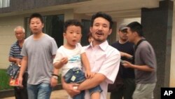 This image taken from video shows Chinese labor activists Hua Haifeng, center, carrying his son, Bobo, and Li Zhao, second from left, leaving a police station after being released in Ganzhou in southern China's Jiangxi province, June 28, 2017. Chinese authorities have released three activists, including Hua and Li, who had been detained after investigating labor conditions at a factory that produced shoes for Ivanka Trump and other brands.