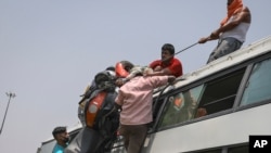 FILE - Indians load a motorcycle on the roof of a bus carrying migrant workers, who are leaving the capital during the COVID pandemic, in New Delhi, India, June 16, 2020.