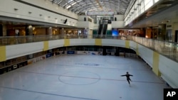 A woman wearing a face mask practices freestyle skating in an ice rink normally crowded with skaters in a shopping mall in Beijing, Sunday, Dec. 18, 2022. 