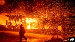 FILE - A firefighter passes a burning home as the Hillside fire burns in San Bernardino, California, Oct. 31, 2019. 