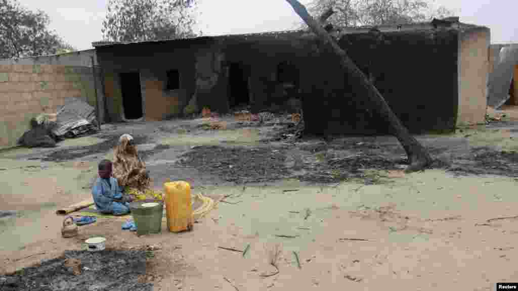 A woman and a child sit on a mat near burnt houses in the aftermath of what Nigerian authorities said was heavy fighting between security forces and Islamist militants in Baga