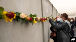 ARCHIVO - Un estudiante coloca una flor en los restos del Muro de Berlín durante una ceremonia conmemorativa para celebrar el 32º aniversario de su caída en Berlín, Alemania, el 9 de noviembre de 2021.