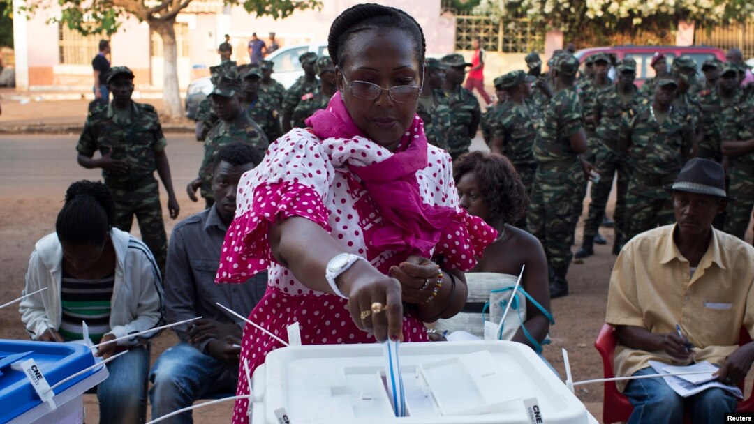 A woman casts her ballot at a polling station as soldiers watch in Bissau, April 13, 2014. 