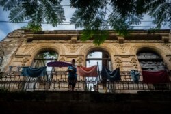 A woman pulls towels off the line after they dried on the balcony of an old home, missing part of its roof, in Havana, Cuba, Nov. 10, 2019.