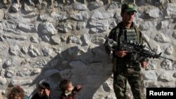 A member of the Afghan security forces stands guard next to family members of ISIS militants who surrendered to the Afghan government in Achin district of Nangarhar province on November 17, 2019. (Parwiz/Reuters)