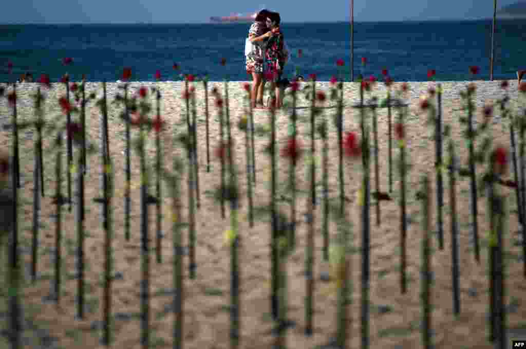 People hug behind roses placed by the NGO Rio de Paz on Copacabana beach, Rio de Janeiro, in memory of Brazil&#39;s half a million COVID-19 victims.