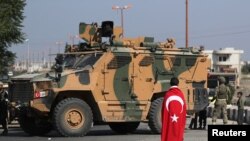 FILE - A boy, with a Turkish flag draped over his shoulders, stands in front of a Turkish military vehicle in the town of Tal Abyad, Syria, Oct. 23, 2019.