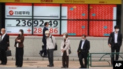 People stand by an electronic stock board of a securities firm in Tokyo, Oct. 19, 2020. Shares advanced in Asia on Monday after China reported its economy grew at a 4.9% annual pace in the last quarter.