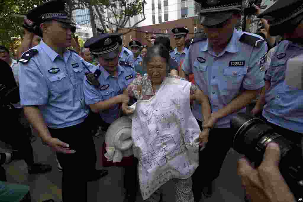 Chinese police officers attempt to remove an elderly woman protesting with the words 'unjust' and details of her own grievances written on a banner outside the Jinan Intermediate People's Court in Jinan, eastern China's Shandong province, August 21, 2013.