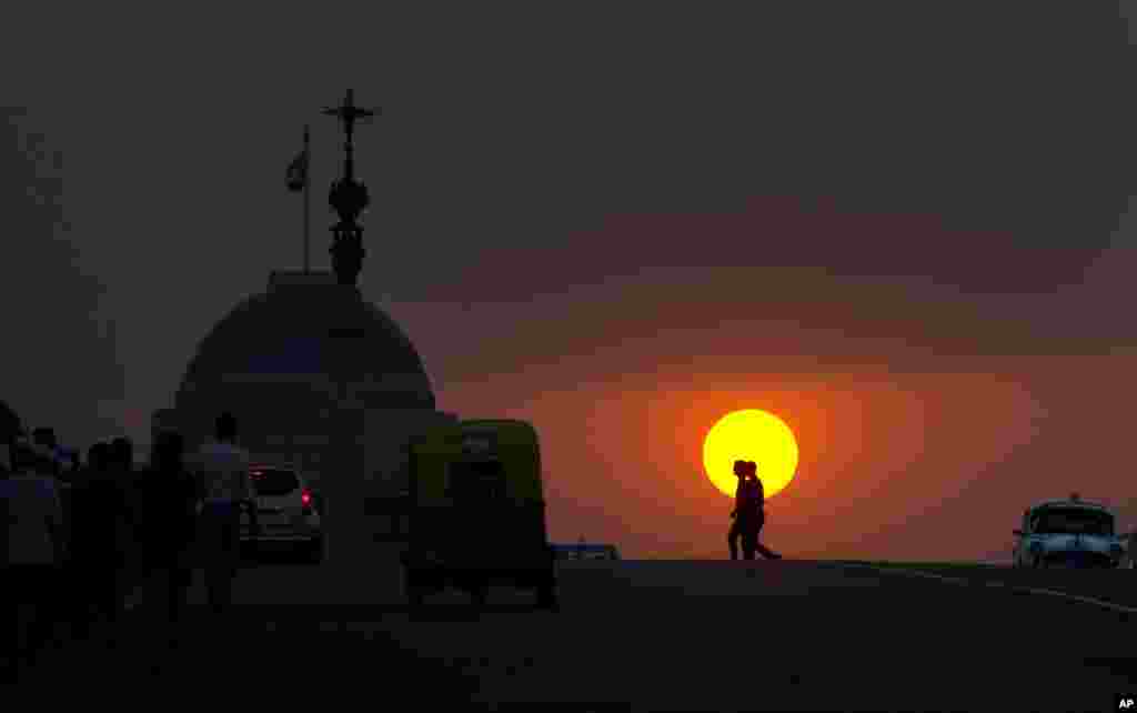 People return from work as the sun sets behind the Indian presidential palace over the Raisina Hill in New Delhi.