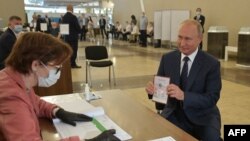 Russian President Vladimir Putin shows his passport to a member of a local electoral commission as he arrives to cast his ballot in a nationwide vote on constitutional reforms at a polling station in Moscow, July 1, 2020. 