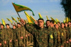 FILE - Hezbollah fighters, holding flags, attend a memorial assembly in Tefahta village, southern Lebanon, Feb. 13, 2016.