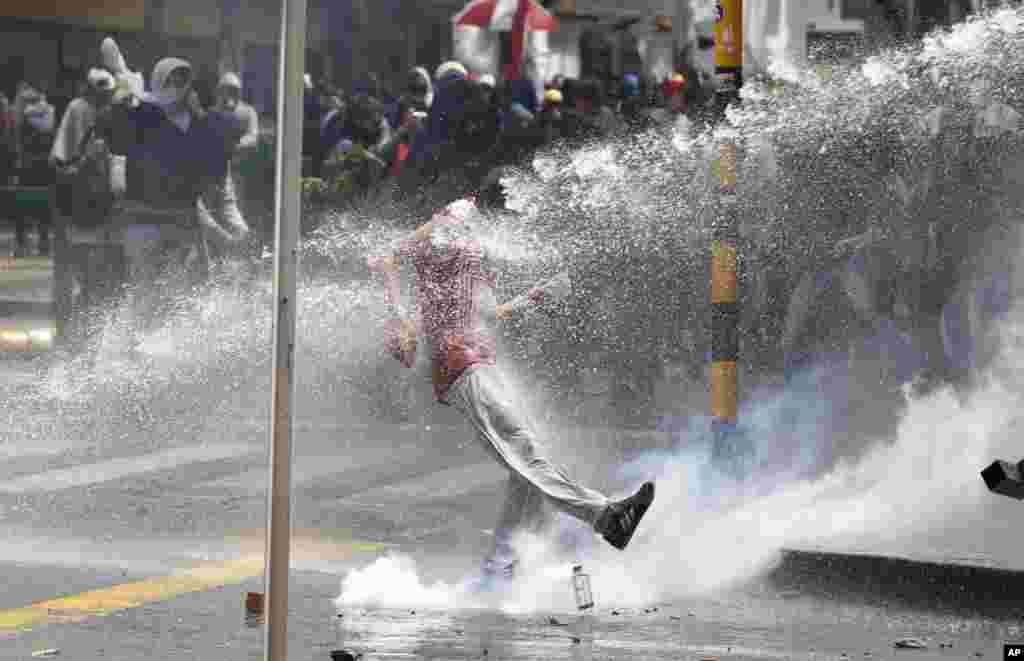 Seorang pengunjuk rasa menendang tabung gas air mata dalam bentrokan dengan polisi anti huru hara yang menggunakan semprotan air di pusat kota Bogota, Kolombia, Agustus 29, 2013.