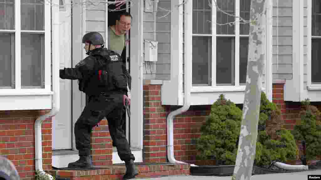 A man looks out of his door as a SWAT team member knocks on his neighbors door as they search for the remaining suspect in the Boston Marathon bombings in Watertown, Massachusetts April 19, 2013.