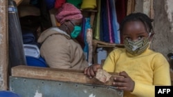 FILE - A fabrics trader and her child wear face masks to guard against the new coronavirus in her shop inside Lilongwe City market in Lilongwe, Malawi, May 18, 2020. 