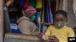 FILE - A fabrics trader and her child wear face masks to guard against the new coronavirus inside her shop in Lilongwe, Malawi, May 18, 2020. 