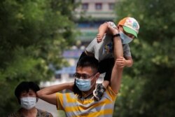 Un hombre con una máscara para protegerse contra el nuevo coronavirus pone a su hijo también con máscara sobre sus hombros mientras visitan un distrito comercial en Beijing, el domingo 19 de julio de 2020.