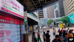 FILE - People wearing a face mask walks past a bank's electronic board showing the Hong Kong share index at Hong Kong Stock Exchange, June 30, 2020. 