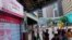 FILE - People wearing a face mask walks past a bank's electronic board showing the Hong Kong share index at Hong Kong Stock Exchange, June 30, 2020. 