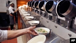 FILE - A worker lifts a lunch bowl off the production line at Spyce, a restaurant which uses a robotic cooking process, in Boston, Massachusetts, May 3, 2018.