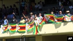 Zimbabweans stand holding flags, during the 36th over of a cricket match between New Zealand and Zimbabwe, at Queens Sports Club in Bulawayo, Zimbabwe, Aug. 6, 2016.