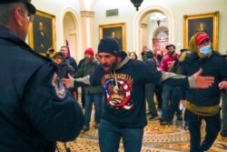 FILE - A man in a QAnon shirt confront U.S. Capitol Police in the hallway outside of the Senate chamber at the Capitol in Washington, Jan. 6, 2021.
