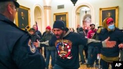 FILE - A man in a QAnon shirt confront US Capitol Police in the hallway outside of the Senate chamber at the Capitol in Washington, Jan. 6, 2021.