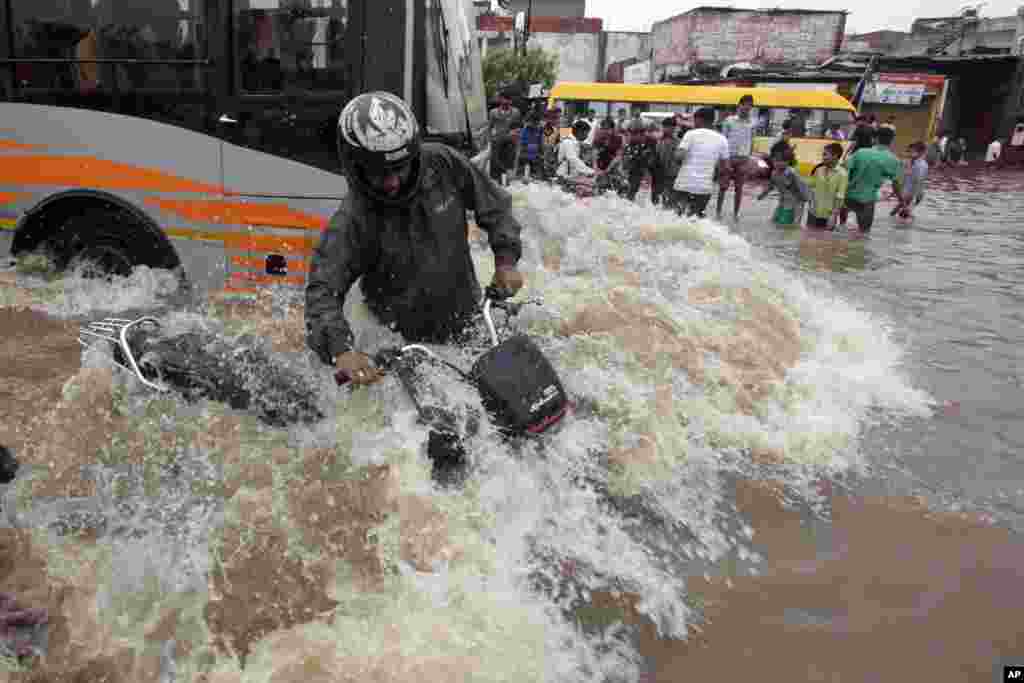 Seorang pengendara motor India mencoba untuk menyeimbangkan kendaraannya sementara sebuah bus melewatinya di jalanan yang banjir di kota Ahmadabad.