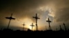 FILE - Iron crosses marking graves are silhouetted against storm clouds building over a cemetery May 25, 2024, in Victoria, Kan.