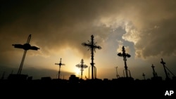 FILE - Iron crosses marking graves are silhouetted against storm clouds building over a cemetery May 25, 2024, in Victoria, Kan.