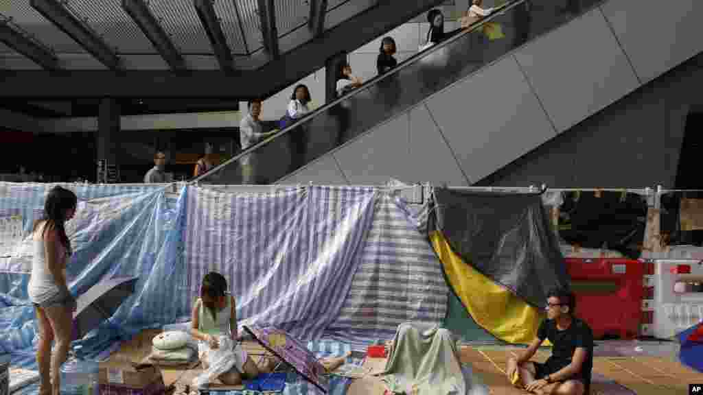 Office workers take an escalator past the pro-democracy student protesters in the occupied areas surrounding the government complex in Hong Kong's Admiralty, Oct. 9, 2014. 