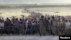 FILE - Turkish soldiers stand guard as Syrians wait behind border fences near the southeastern town of Suruc, Sanliurfa province, Sept. 2014.