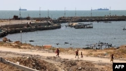 امریکی سینٹرل کمانڈ (CENTCOM) کی طرف سے اعلان کردہ "بحری راہداری" کے ایک حصے کے طور پر ساحل سے بحریہ کے جہاز نظر آرہے ہیں۔ فلسطینی غزہ شہر میں ایک جیٹی سے گزر رہے ہیں۔ امریکی سینٹرل کمانڈ کا فراہم کردہ فوٹو