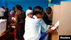 Hooyo cunugeeda xanbaarsan oo cokeeda ka dhiibanaysa goob codbixin oo ku taalla magaalada Gatundu ee dalka Kenya.
