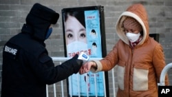 A woman wearing a protective face mask receives a temperature check from a security guard as she enters Qianmen Street, a popular tourist spot, in Beijing, Feb. 16, 2020. 