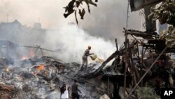 Un homme jette de l'eau sur les restes fumants des étals du marché après un incendie durant la nuit sur le marché en plein air de Gikomba à Nairobi, au Kenya, mardi 23 juin 2015.