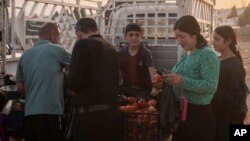 Residents buy vegetables at a market inside the Sharya displacement camp in the Duhok area of the Kurdistan region of Iraq during sunset, June 21, 2024.